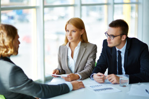 Two serious business partners listening attentively to young man at meeting in office