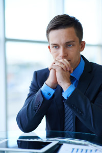 Sad businessman sitting at workplace and trying to find solution of problem