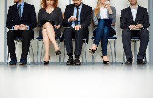 Line of young people sitting by wall while waiting for their turn for interview